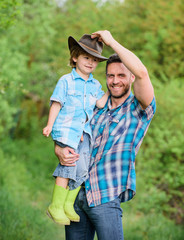 Wall Mural - Growing cute cowboy. Weekend at farm. Little boy and father in nature background. Spirit of adventures. Little helper in garden. Child having fun cowboy dad. Farm family. Holidays at parents farm