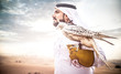 Arabic man with traditional emirates clothes walking in the desert with his falcon bird