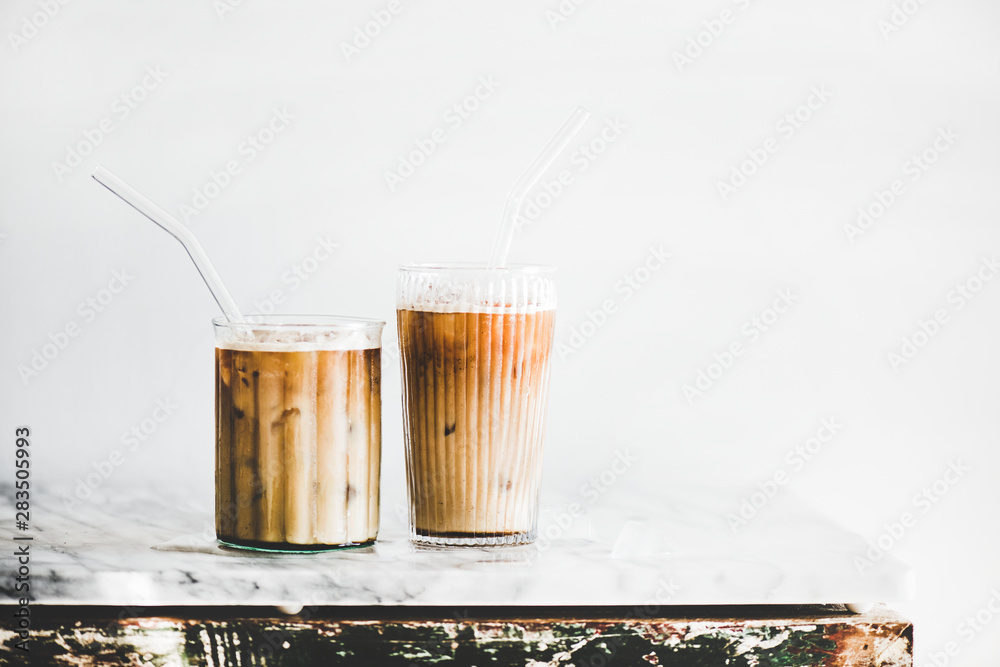 Homemade iced latte coffee in glasses with straws on grey marble table, white wall at background, copy space. Summer cold refreshing drink concept - obrazy, fototapety, plakaty 