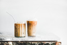 Homemade Iced Latte Coffee In Glasses With Straws On Grey Marble Table, White Wall At Background, Copy Space. Summer Cold Refreshing Drink Concept
