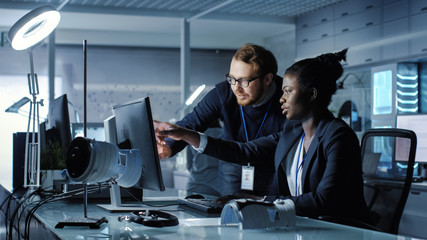 Wall Mural - african american female scientist works on a computer caucasian male colleague joins her with work r