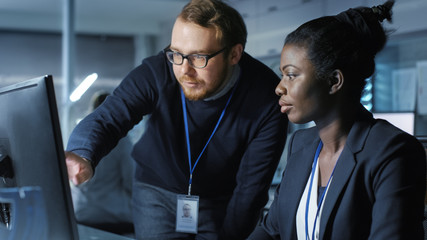 Wall Mural - african american female scientist works on a computer caucasian male colleague joins her with work r
