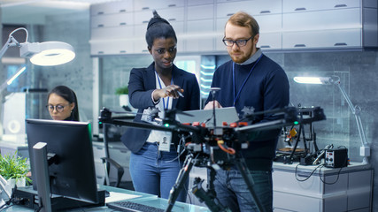 Wall Mural - caucasian male and black female engineers working on a drone project with help of laptop and taking 