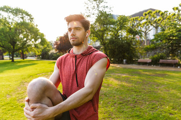 Poster - Photo of calm man using earphones and doing exercise while working out in city park