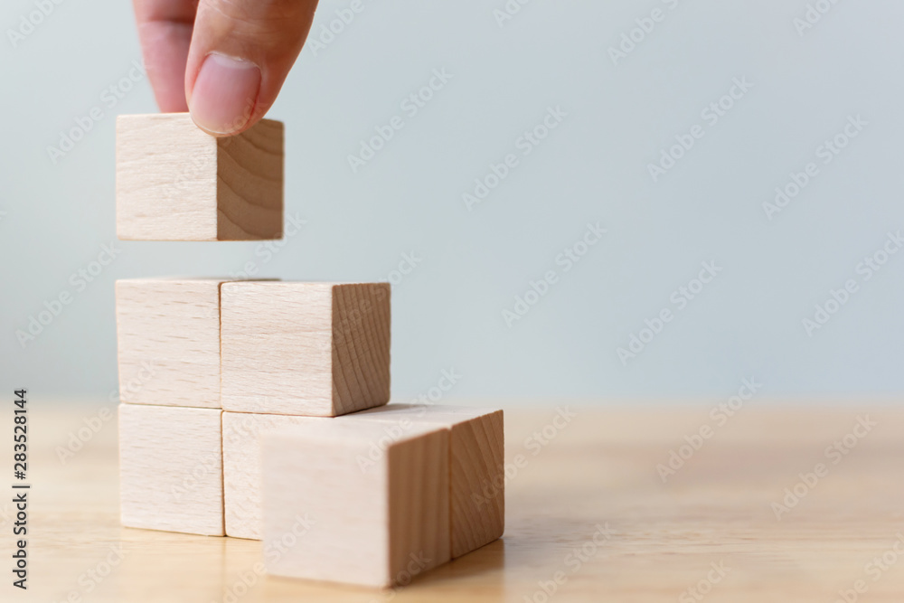 Hand arranging wood block stacking as step stair on wooden table. Business concept for growth success process. Copy space - obrazy, fototapety, plakaty 