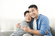 © nuiiko - Asian mother hugging her son and sitting on sofa at home, lifestyle concept.