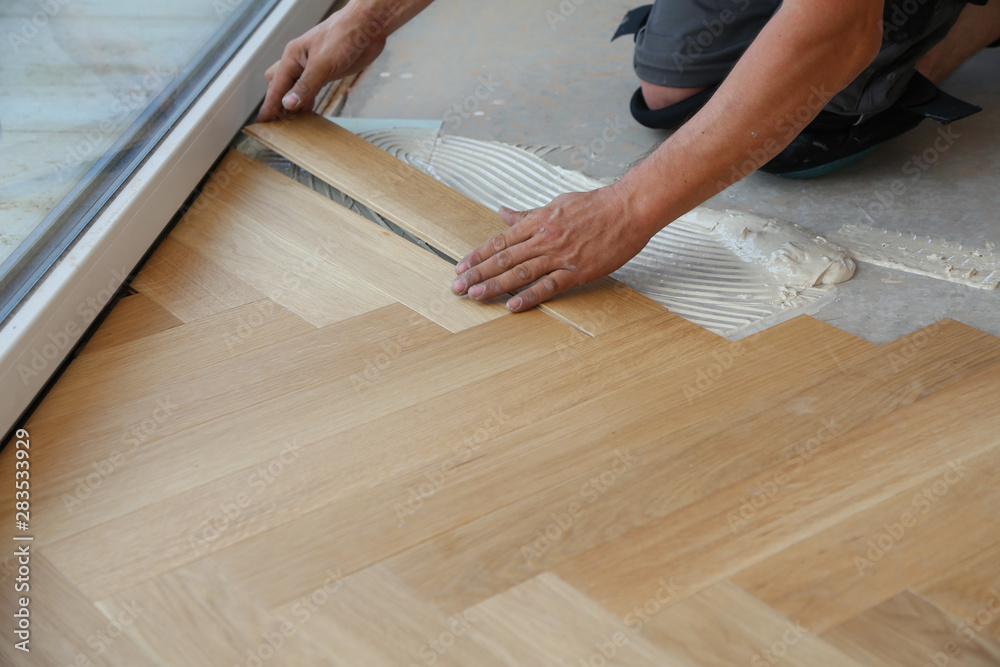Worker laying parquet flooring. Worker installing wooden laminate flooring - obrazy, fototapety, plakaty 