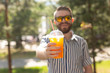 © satura_ - Portrait of a positive cheerful young man with a glass of juice with a straw while walking in the park on a warm sunny summer day. The concept of rest after study and work on weekends.