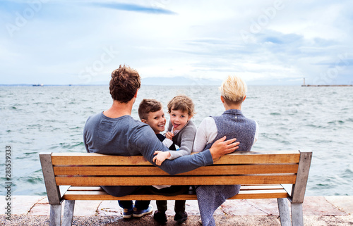 Young Family With Two Small Children Sitting On Bench Outdoors On