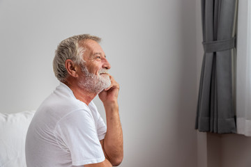 Senior elderly man sitting on bed and thinking after waking up in morning