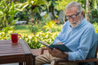 © wirojsid - Senior elderly man reading book with mug of coffee in garden