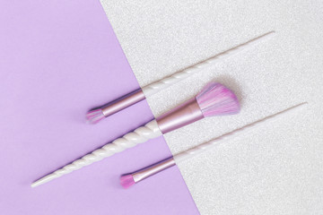 Wall Mural - Three unicorn makeup brushes on trendy pastel silver lilac violet background. Flat lay with copy space, beauty and cosmetics blogger concept