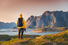 A traveler in a yellow jacket looks at the sunset on the Lofoten Islands, traveling to Northern Norway, a beautiful bright landscape