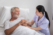 © wirojsid - Happy nurse holding elderly man hands with blanket in bedroom at nursing home