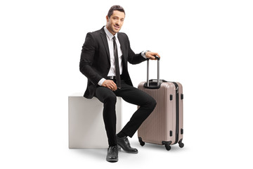 Sticker - Businessman with a suitcase sitting on a white cube and looking at the camera