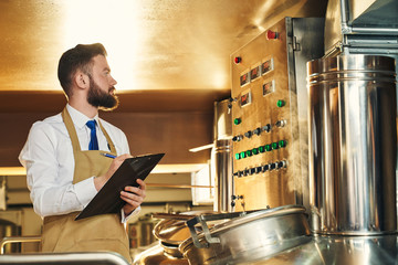 Young bearded man controlling process of beer manufacturing