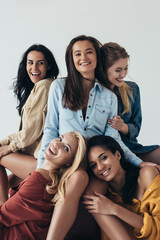 Wall Mural - front view of five smiling attractive multiethnic feminists in colorful shirts embracing and looking at camera isolated on grey