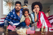 © Mediteraneo - Happy African American family of three watching tv and cheering sport games on sofa at home