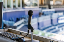 Microphone Resting In Holder On Desk Of Announcers Booth For Baseball Stadium.