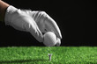 Player putting golf ball on tee against black background, closeup