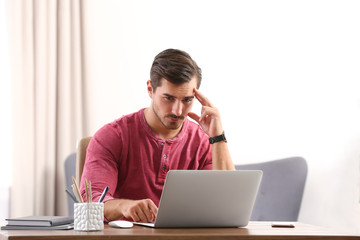 Handsome young man working with laptop at table in office