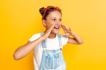 Wall Mural - Portrait of a happy teenager, girl screaming good news at camera, standing on yellow background