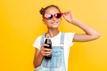 Wall Mural - Happy teen girl resting on a yellow background with a refreshing drink in hand