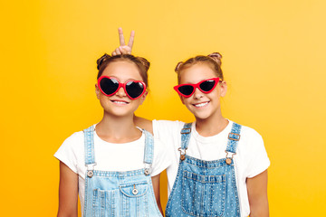 Two teenage girls, girlfriends in sunglasses posing on a yellow background