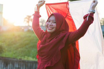 portrait of young asian muslim woman with scarf lift the red and white flag into the air