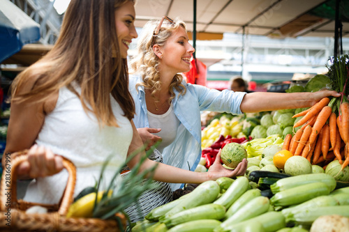 Fotomural Young happy women shopping vegetables and fruits on the market
