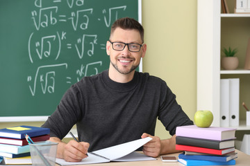 Wall Mural - Handsome male teacher sitting at table in classroom