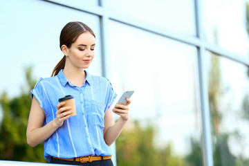 Wall Mural - Young businesswoman with cup of tasty coffee and mobile phone outdoors