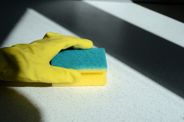 Hand in yellow rubber glove washing kitchen surface lit by the sun. Home cleaning