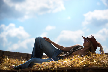 Beautiful cowgirl. Shot in the stables on the hay on a background of clear sky