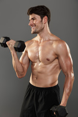 Sticker - Cheerful happy handsome young strong sportsman posing isolated over grey wall background make exercises with dumbbells for arms.