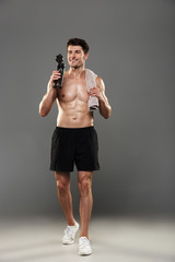 Poster - Handsome young strong sportsman isolated over grey wall background holding towel and bottle with water.