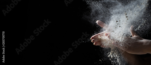 Fotomural woman chef hand clap with splash of white flour and black background with copy space