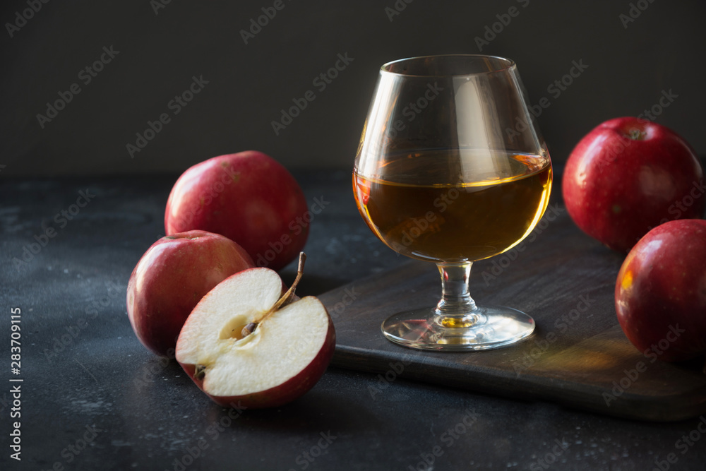 Glass with Calvados brandy and red apples on black. Close up. - obrazy, fototapety, plakaty 