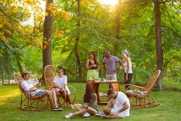 Wall Mural - Group of happy friends eating and drinking beers at barbecue dinner on sunset time. Having meal together outdoor in a forest glade. Celebrating and relaxing. Summer lifestyle, food, friendship concept