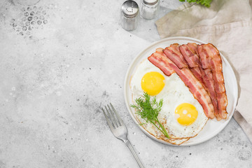 Scrambled eggs with bacon in a white plate on a grey table. Breakfast