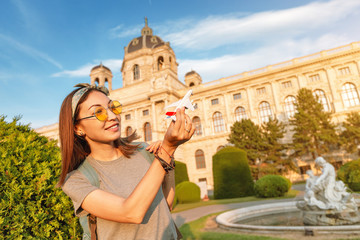 Wall Mural - Happy young Asian girl with a toy airplane posing against the backdrop of a historic building in a European city. Travel and Air tourism transport Concept