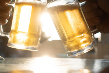 Closeup toast clinking fresh lager beer glasses mugs with sun rays in hot summer day