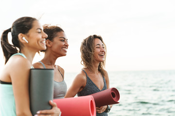 Wall Mural - Three cheerful young sport girls standing at the beach