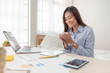 © weedezign - Asian businesswoman drinking coffee and while working with laptop on table in bedroom at home.Work at home concept.work from home concept