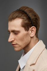 Cropped close-up shot of a young chestnut European man with a black hairband made in the form of a figured spiral spring twining around the wire in his hair. The fashion model with an unshaved chin 