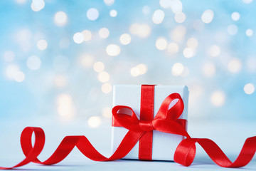 christmas gift box or present box with beautiful red ribbon against holiday lights background.