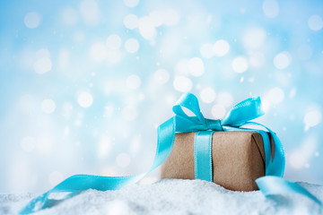 Beautiful winter composition with Christmas gift or present box in snow against holiday lights background.