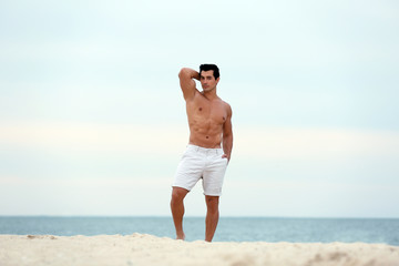 Wall Mural - Handsome young man posing on beach near sea