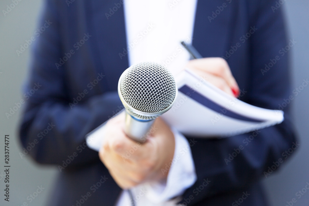 Female journalist at news conference or media event, writing notes, holding microphone - obrazy, fototapety, plakaty 