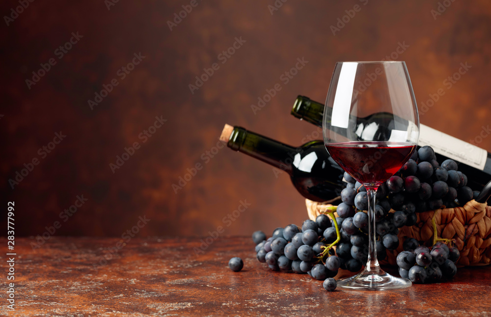 Juicy blue grapes and bottles of red wine on a brown background. - obrazy, fototapety, plakaty 